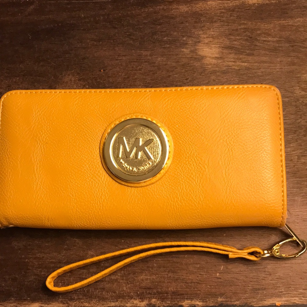 Warm, ochre-colored wristlet that says Michael Kors. Gold monogram. See pics.